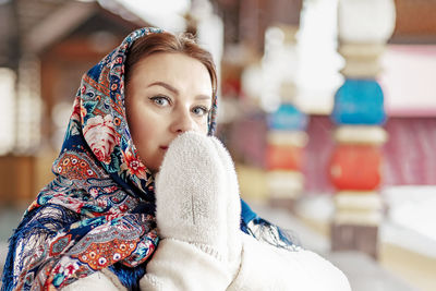 A slavic woman in a national colored scarf,a fur coat and  mittens on the porch of a wooden house