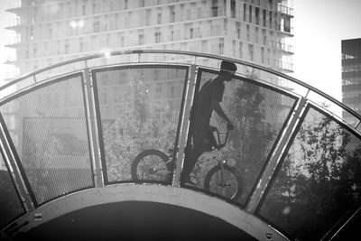 Low angle view of boy riding bicycle on bridge against building