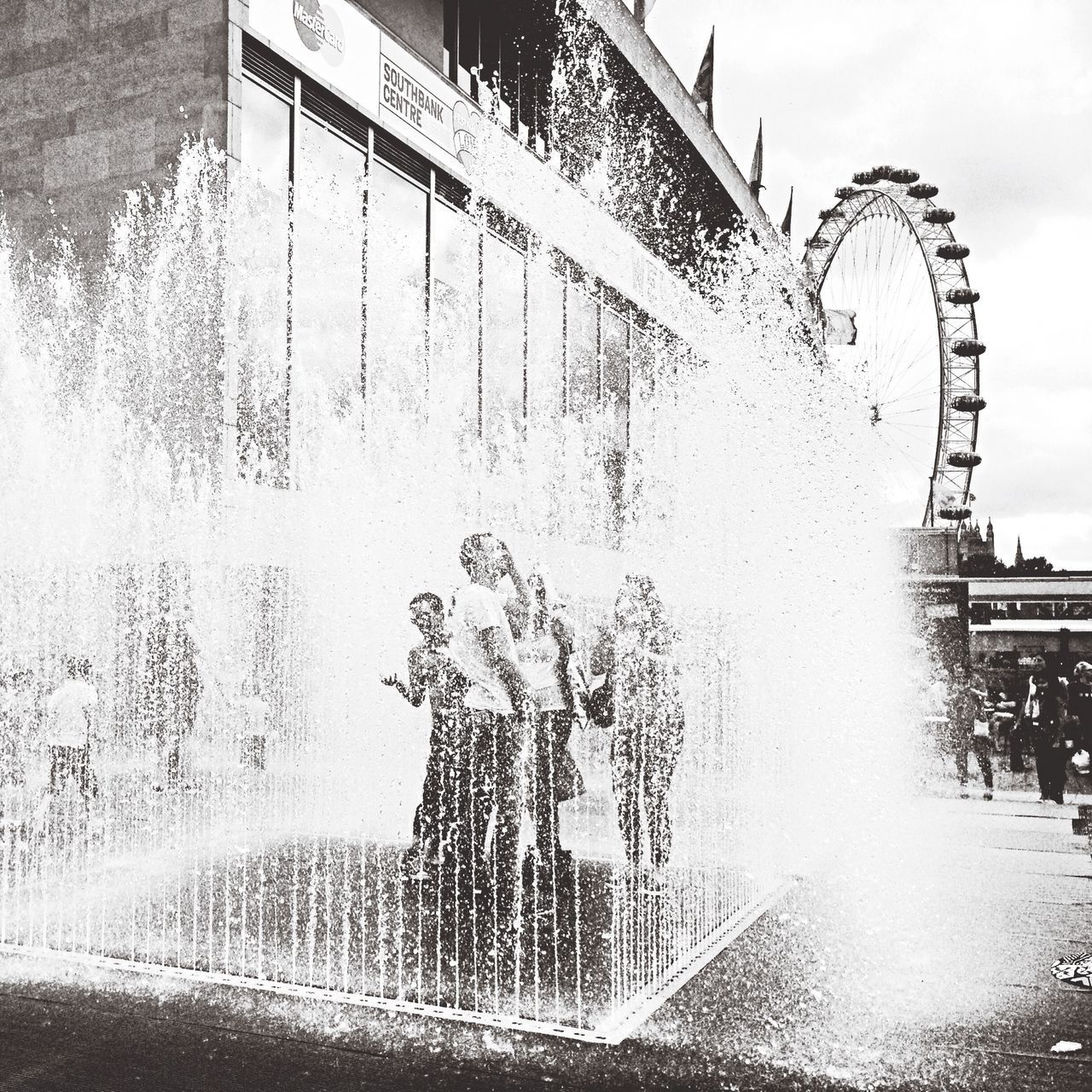 building exterior, architecture, built structure, water, city, fountain, sky, wet, reflection, motion, building, drop, rain, spraying, day, outdoors, splashing, weather, puddle, low angle view