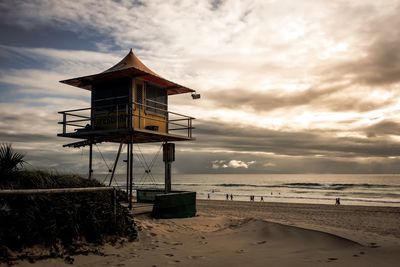 Lifeguard hut on beach against cloudy sky during sunset