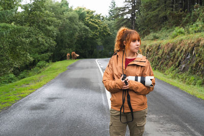 Red-haired female photographer taking photos of nature on the road with horses in the background