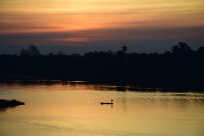 Silhouette trees by lake against orange sky