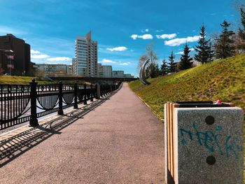 Footpath by railing in city against sky