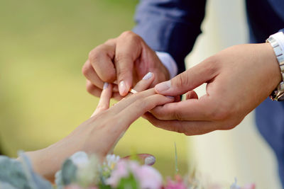 Cropped image of bridegroom putting ring in fingers of bride