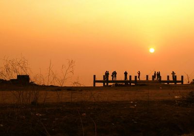 Silhouette people standing on field against orange sky