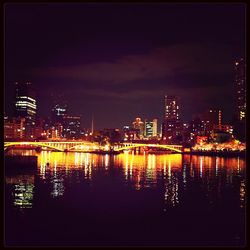 Illuminated buildings by river against sky at night