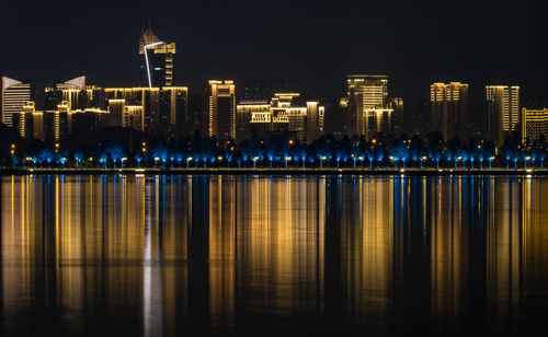 Illuminated buildings by river against sky at night