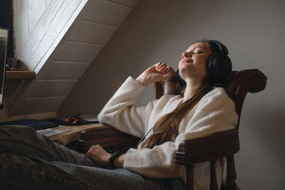 Young woman listening to music in big headphones near computer at home. creating play list, enjoying