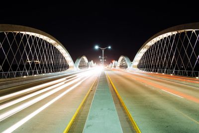 Light trails on illuminated bridge against sky at night