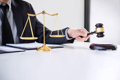 Midsection of lawyer striking gavel on table