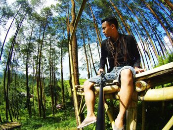 Low angle view of man sitting on bench at forest