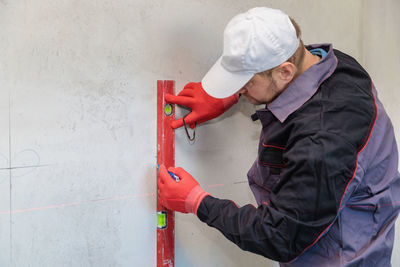 A man, an electrician marks out holes for sockets with a pencil, a tape measure