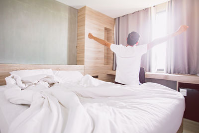 Rear view of man stretching hands on bed at home
