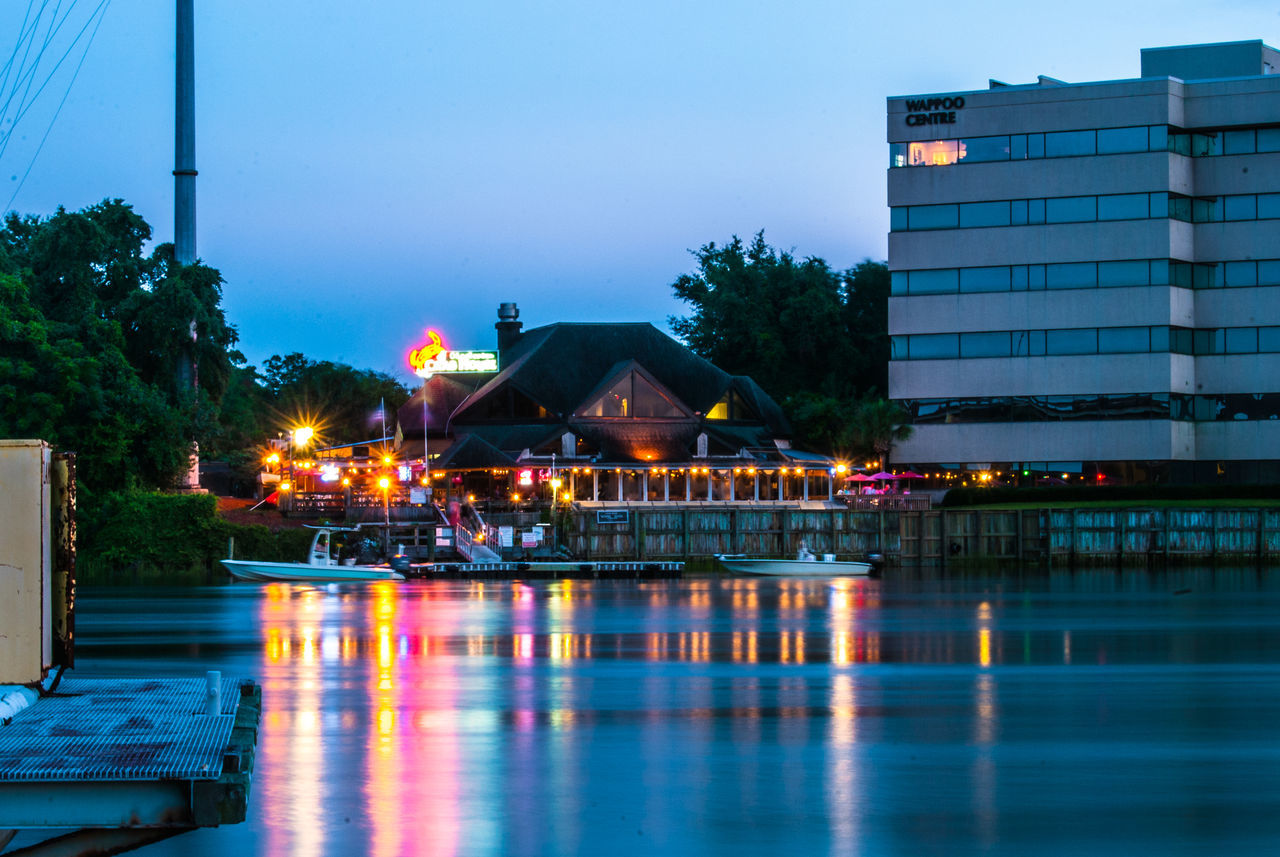 illuminated, water, built structure, architecture, building exterior, reflection, waterfront, street light, blue, clear sky, night, lighting equipment, tree, sky, city, swimming pool, river, dusk, outdoors, lake