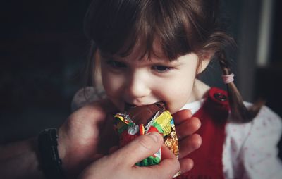 Cropped hands of father feeding chocolate to daughter at home