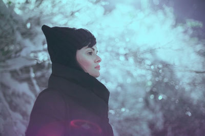 Side view of woman looking away while standing outdoors during winter