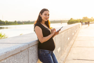 Portrait of young woman standing on mobile phone against sky