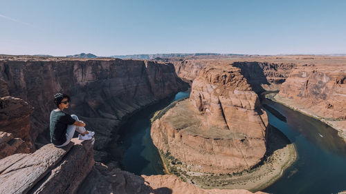 Full length of woman sitting on cliff against sky