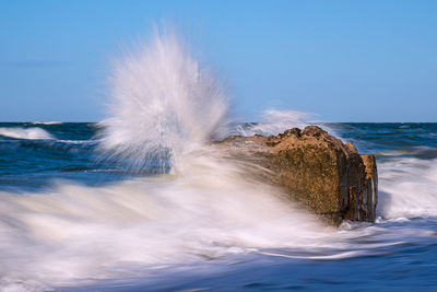 Sea waves splashing on shore against clear sky