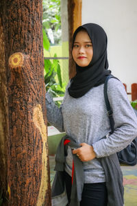 Portrait of woman standing by tree trunk