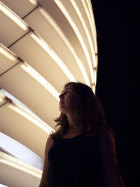 Young woman standing by illuminated lamp at night