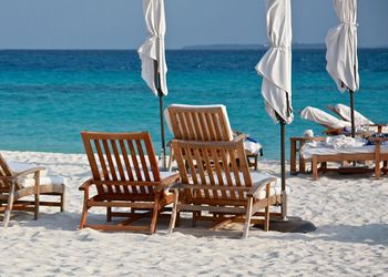 Lounge chairs and umbrellas at beach against sky on sunny day