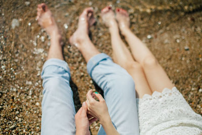 Low section of couple sitting on shore at beach