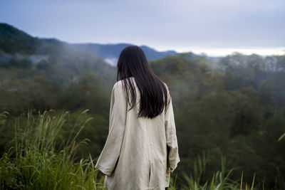 Rear view of woman standing on field looking at foggy