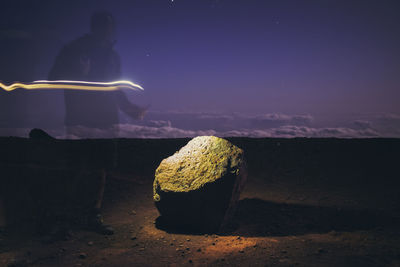 Silhouette person on rock by sea against sky at night