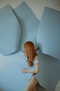 Side view of woman with blue papers standing against wall
