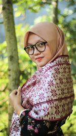 Portrait of smiling woman standing against trees