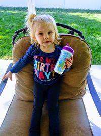 Portrait of cute baby girl holding bottle while sitting on chair