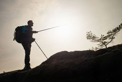 Hiker on peak in target with trekking poles in hand in air. man in black trousers and blue jacket