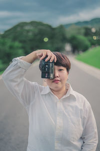 Young woman photographing with camera while standing on road