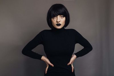 Portrait of female model standing with arms akimbo against gray background