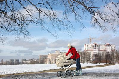 Woman with baby carriage on street against building during winter
