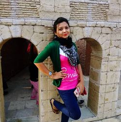 Portrait of smiling young woman standing against wall