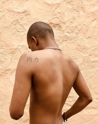 Rear view of shirtless man standing against wall