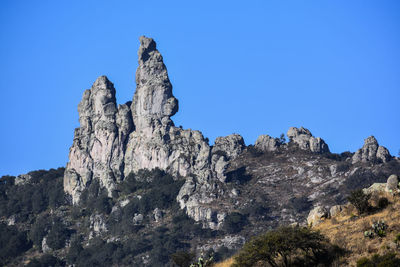 Low angle view of rocky mountains against clear blue sky