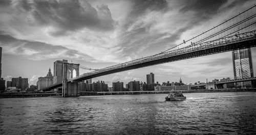 View of suspension bridge over river against cloudy sky