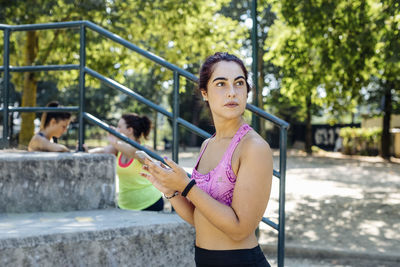 Young sportswoman with smartphone standing in park