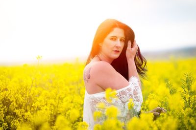 Beautiful young woman standing by yellow flower field