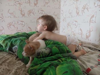 Shirtless girl playing with cat on bed at home