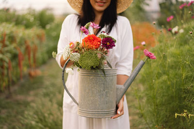 The girl is holding a watering can with flowers in her hands. the bouquet is in focus.