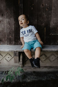 Cute boy looking away while sitting against wall