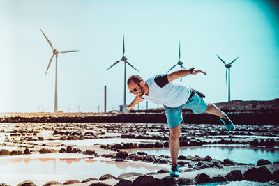 Happy man with arms outstretched balancing on rocks against windmills