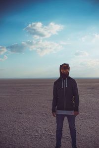 Man wearing mask while standing at beach against blue sky