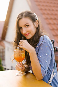 Young attractive woman is sitting at a table in a summer cafe and drinking a cocktail