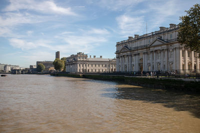 Buildings at waterfront against cloudy sky