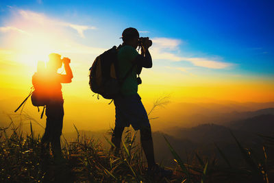 Silhouette man photographing against sky during sunset